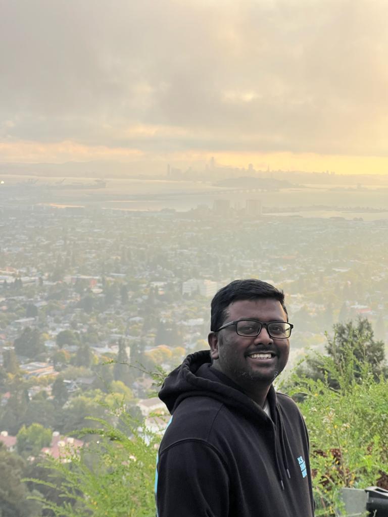 Muthamil selvan smiling in a red plaid shirt and tortoise shell glasses